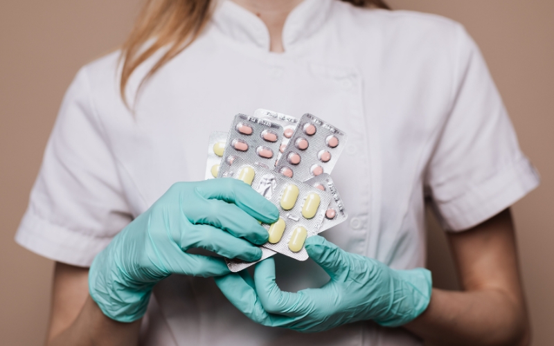 Healthcare professional in a white uniform shirt and green gloves carries a handful of birth control pills.